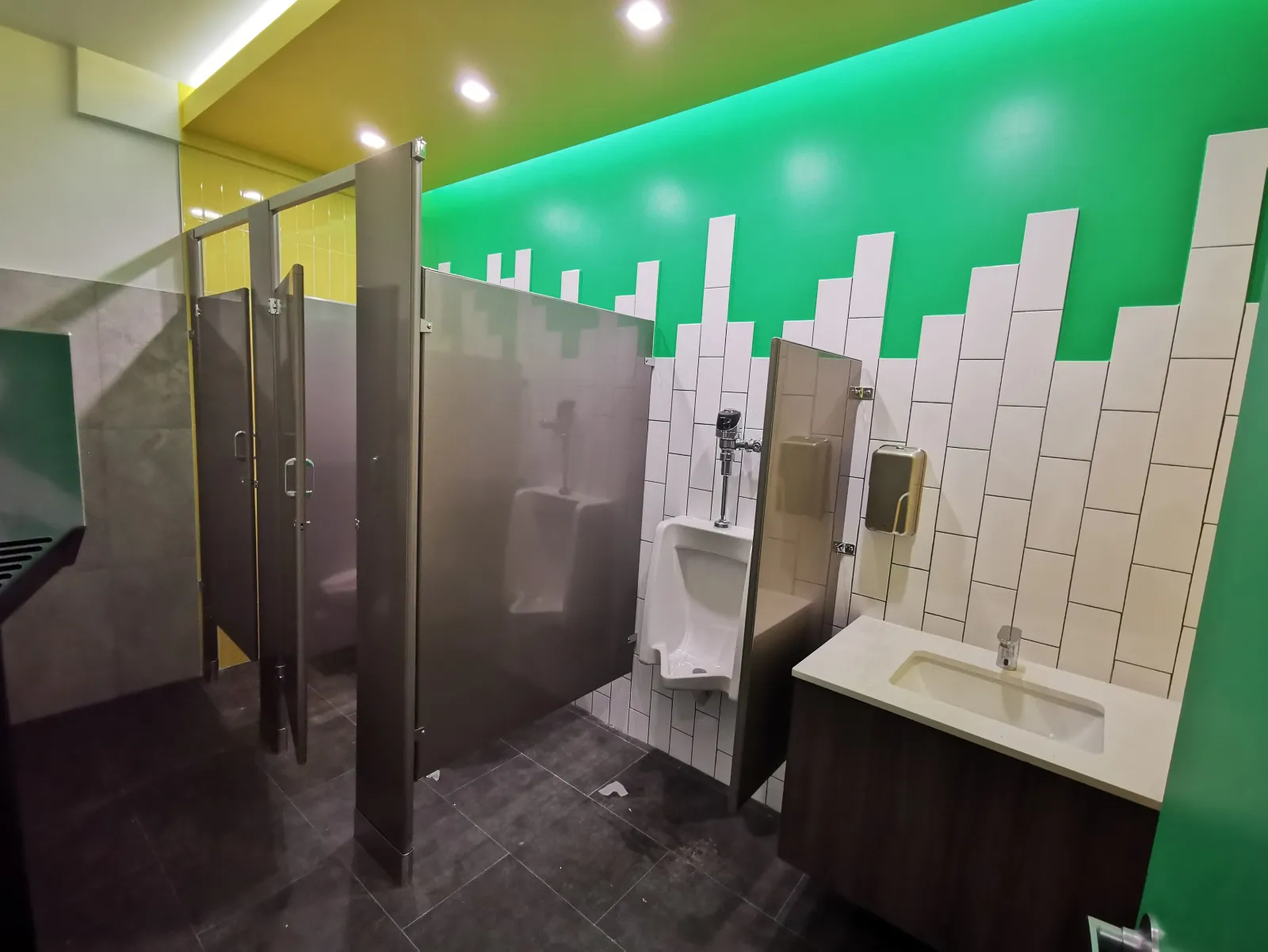 475 East 57th Street — Restroom rebuilt from worn gray partitions to color-blocked tile with new stalls and fixtures — after