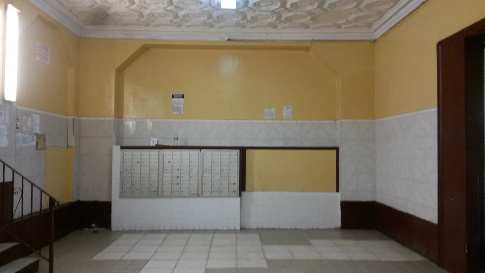 1055 Jerome Avenue — Dated lobby with tile wainscot and worn finishes reborn as a marble-floored common area with a stone mailbox feature wall. — before
