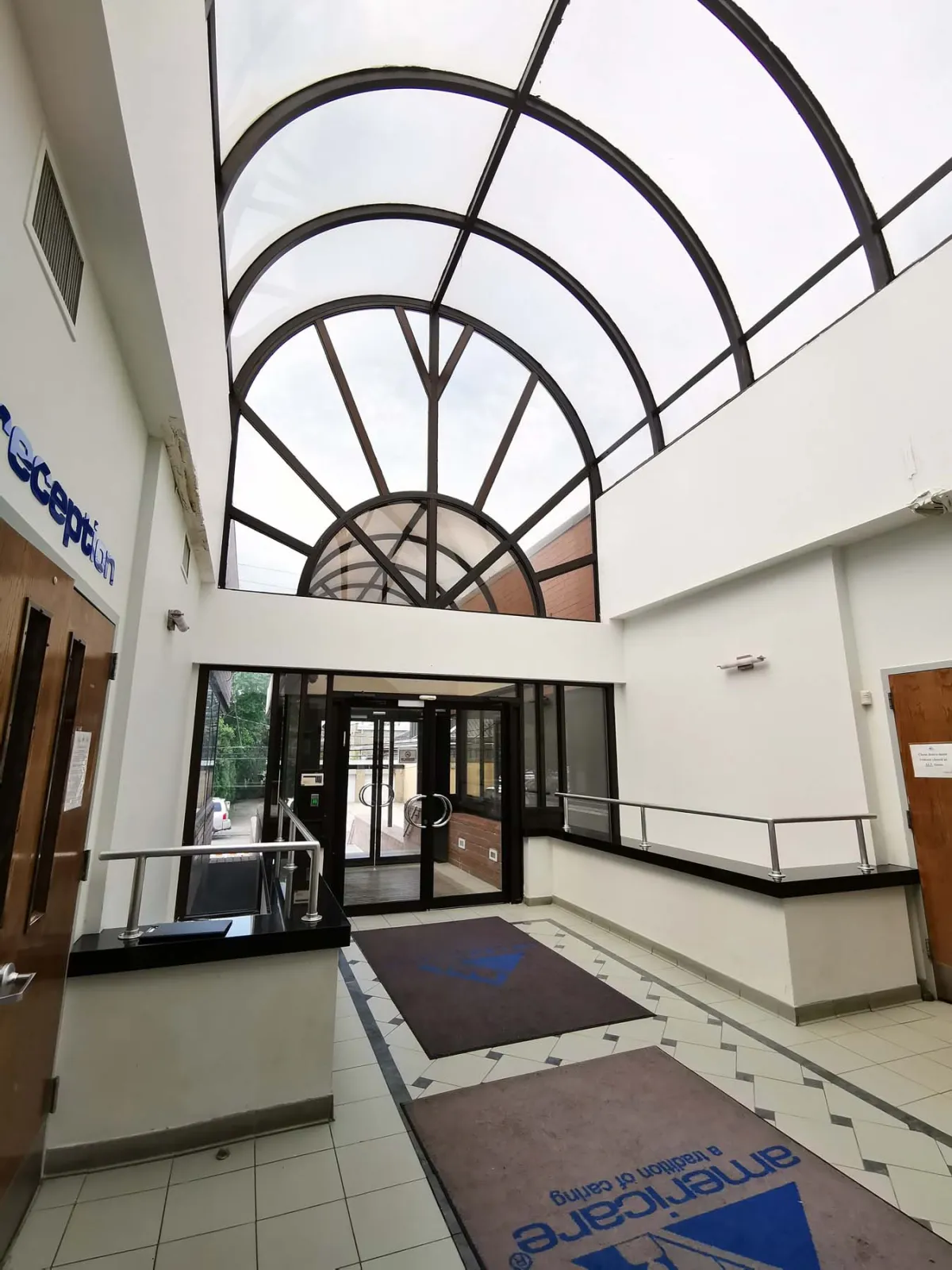2275 Coleman Street — Skylight reception atrium — original tile and matting transformed into a modern lobby with steel beams, wood-slat ceiling, and feature wall — before